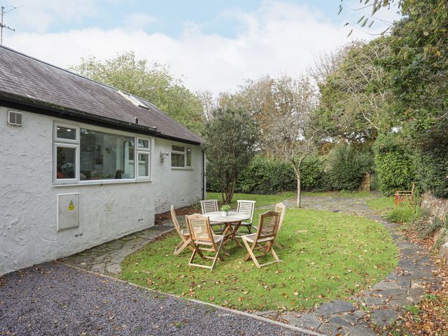 An outdoor garden area with wooden chairs and a table on grass next to a white building at Ty Cerrig in Llanbedrog
