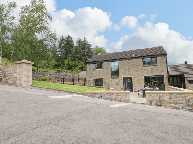 A stone house with a tiled roof a patio area with a table and chairs and a lawn with trees at Ty Gambo in Oker near Matlock