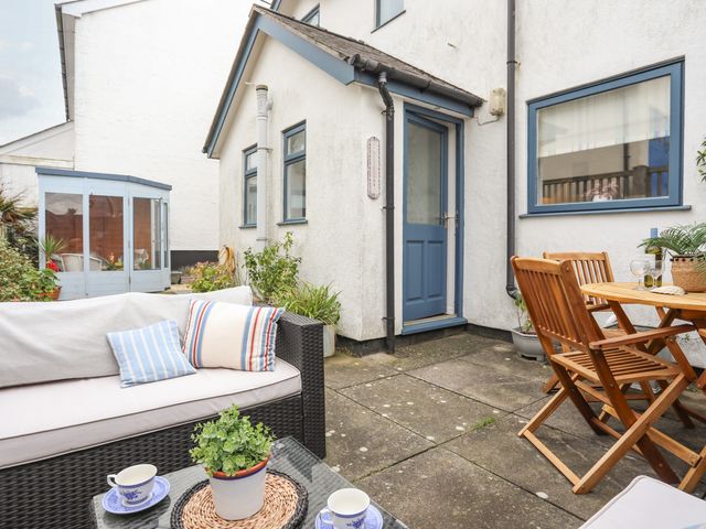 An outdoor patio with wicker sofa and wooden table and chairs outside a white house with blue door and window frames at Wingelock in Rhosneigr