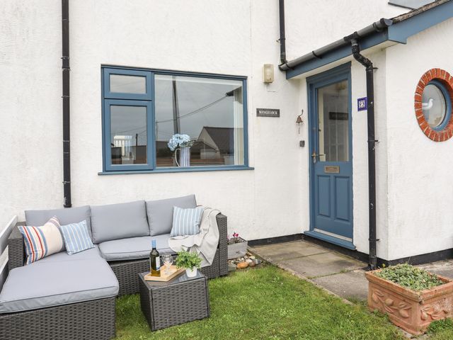 An outdoor seating area with a wicker sofa and cushions near a blue door and window at Wingelock in Rhosneigr