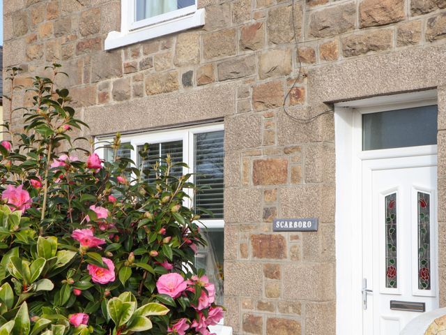 A stone exterior wall with a white door and window and pink flowers in front at Scarboro in Redruth