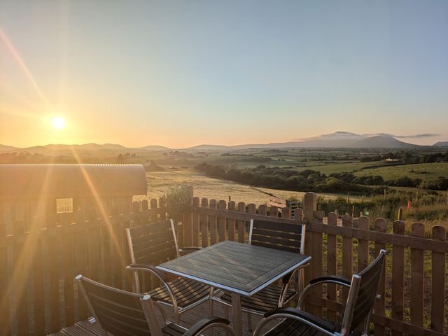 An outdoor seating area with a table and four chairs on a wooden deck overlooking fields and hills at Hafan Gelli Sheperds Hut - Enlli in Pwllheli