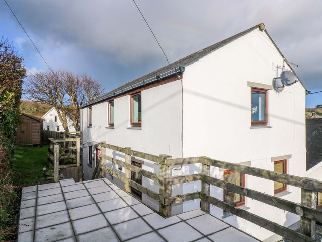 A white two-story house with wooden window frames and a tiled patio with wooden railing in a garden at Little Fernleigh in Coverack