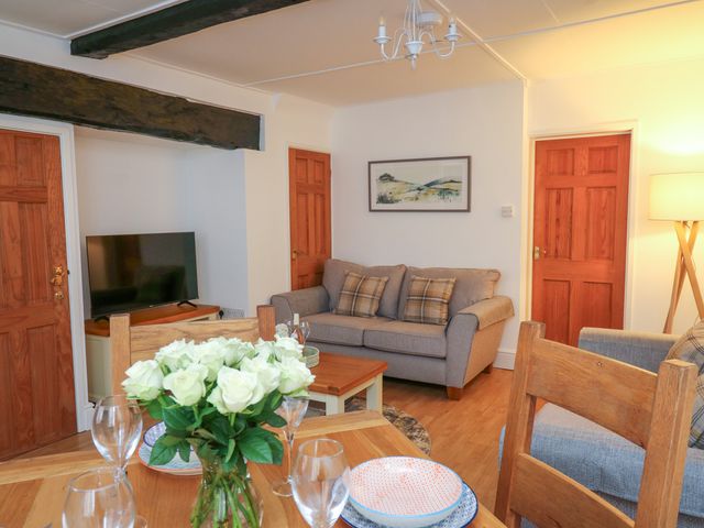 A living room with a gray sofa and wooden dining table with plates and a vase of white flowers at 1 Penporth in Rhayader