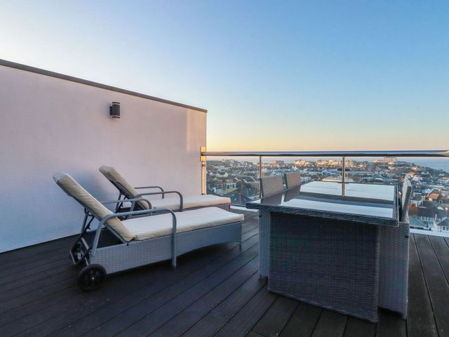 A rooftop terrace with two lounge chairs and a dining table with chairs overlooking a coastal town at 10 Quay Court in Newquay