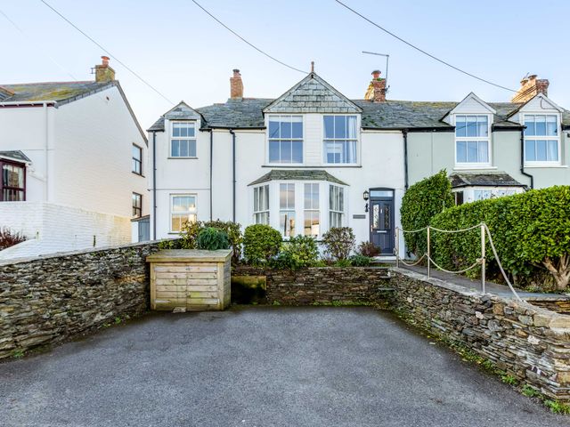 A front view of a white terraced house with bay windows stone walls and a paved driveway at Tre Lowen in Port Isaac