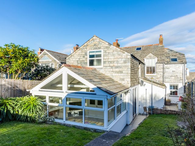 A stone house with a white conservatory and garden in the foreground at Tre Lowen in Port Isaac