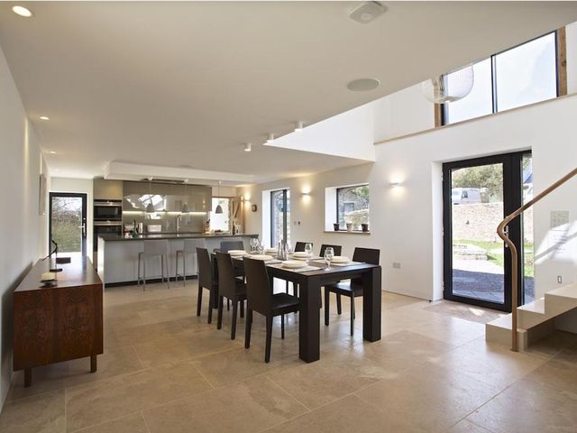 A dining area with a table set for six and an open kitchen with bar stools at The Milking Shed in Bantham