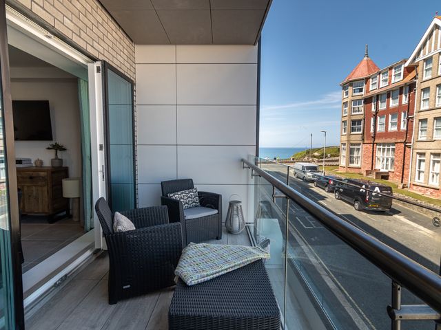 A balcony with black wicker chairs and a glass railing overlooking a street and a building with a sea view at 31 Cliff Edge in Newquay