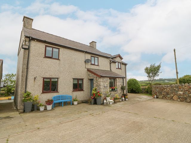 A two-story house with stone and stucco exterior with several flower pots and a blue bench in front at Tyn Rallt Ice Cream Farm in Malltraeth near Newborough