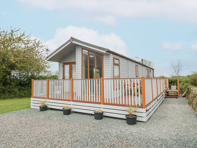 A single mobile home with wooden deck and potted plants on gravel at Y Caban in Brynsiencyn