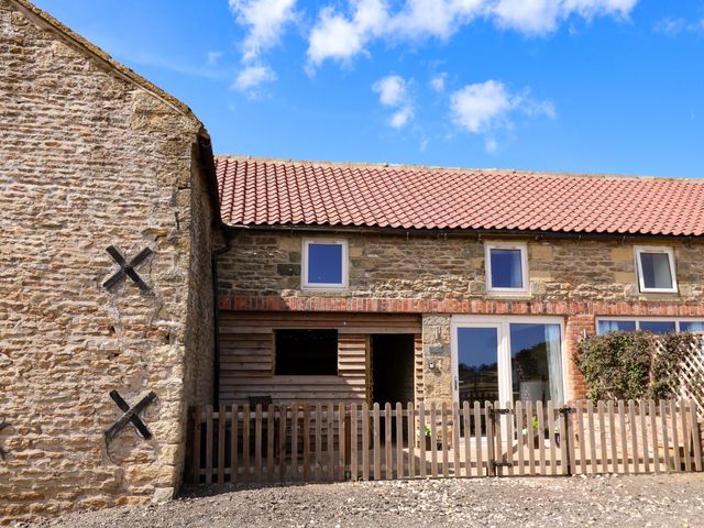 An outdoor view of a stone building with windows and a wooden fence at Hawthorn Cottage in Silpho near Scalby