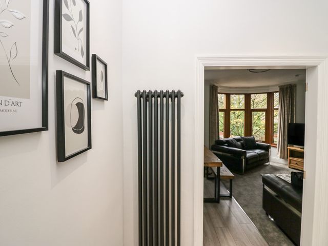 A hallway with black and white framed artwork above a black radiator leading to a living room with leather sofas and large windows at Eden on the Crescent in Bare near Morecambe