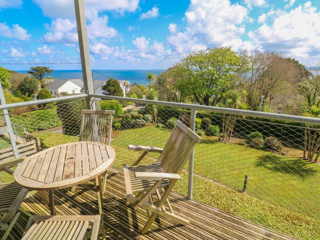 A balcony with wooden chairs and a table overlooking a garden and the sea at Talland View in St Ives