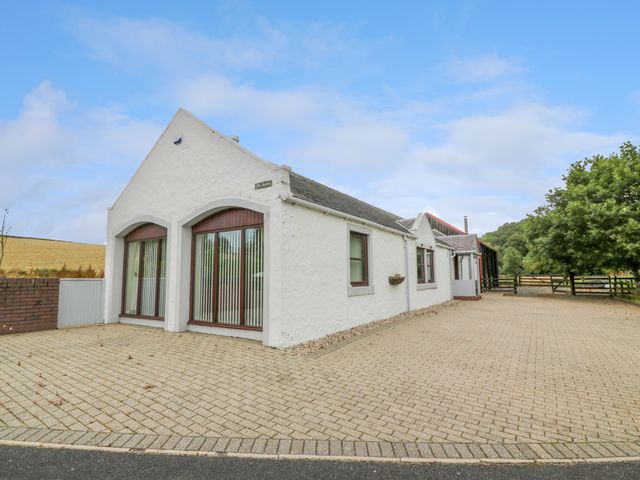 A white single-story building with large windows and a paved driveway at The Stables at Daldorch in Tarbolton