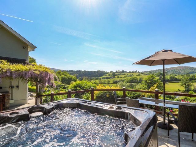 An outdoor patio with a hot tub table umbrella and chairs overlooking green fields at Curtau Llanfaredd near Builth Wells