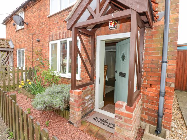 A brick house entrance with a wooden porch and a blue door partially open at Easter Cottage in Dersingham