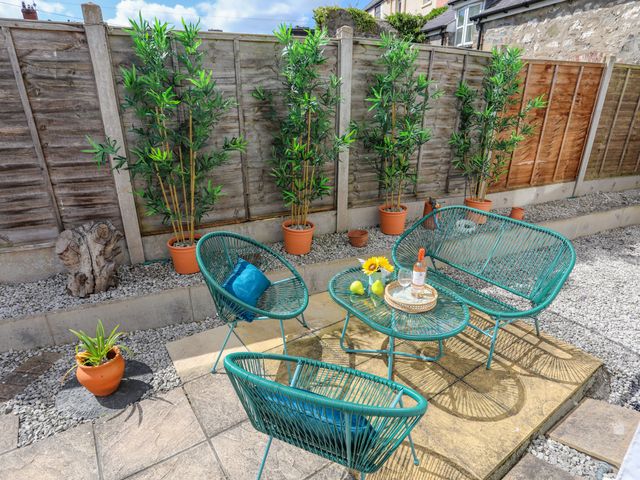 An outdoor patio with teal chairs and table surrounded by potted plants and a wooden fence at 1 Tyn Y Gongl Cottage in Beaumaris