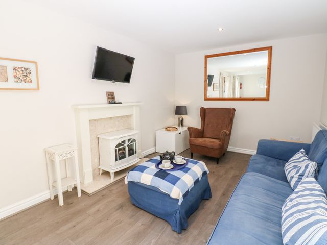 A living room with a blue sofa and ottoman with a checkered cloth a brown armchair a wall-mounted tv and a white fireplace at Elder Cottage in Caldwell near Eppleby