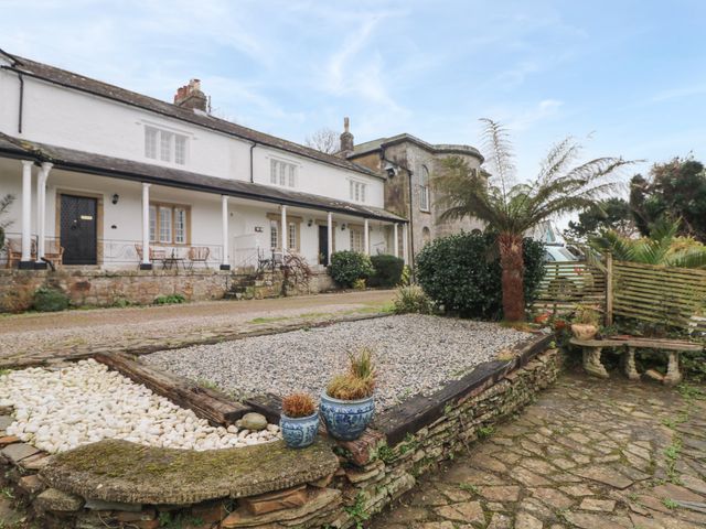 A stone paved courtyard with a gravel garden and potted plants in front of a white building with a porch at Josie in Pentewan