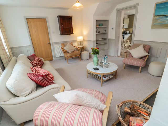 A living room with sofas armchairs a coffee table and a basket of firewood at Eider Cottage in Warkworth