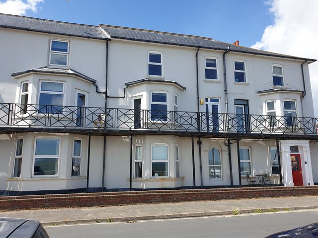 A two-story white building with multiple windows and balconies and a red door at 11 The Craighurst in Southwold