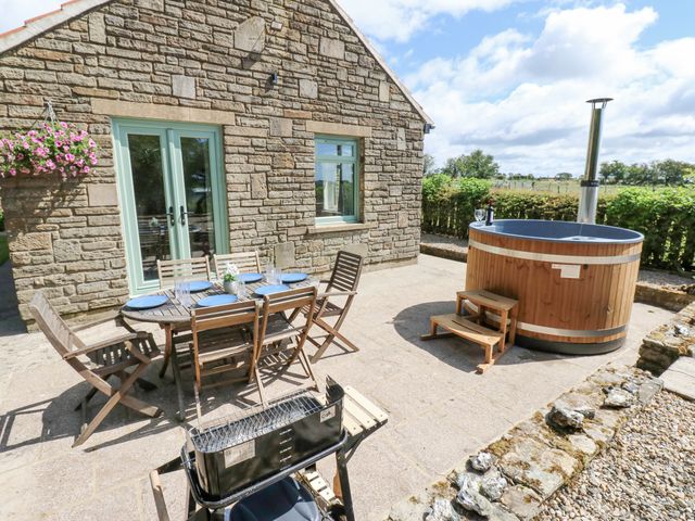 An outdoor patio with a wooden dining table and chairs a hot tub and a barbecue grill at Thornfield in Windmill