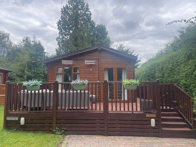 A lodge with a deck and outdoor furniture at Bowness Bay Lodge, Oakside 16, Fallbarrow Park near Bowness-On-Windermere