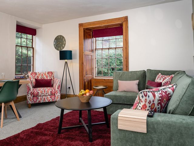 A living room with green and patterned seating a black round coffee table wooden framed windows and a red rug at Watermouth Castle Rhododendron Apartment in Berrynarbor near Ilfracombe