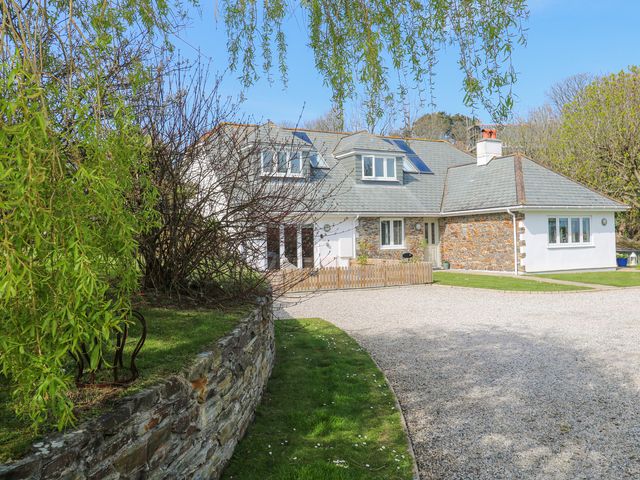 A stone house with a gravel driveway and green lawn surrounded by trees at Mariners Rest in Gorran Haven