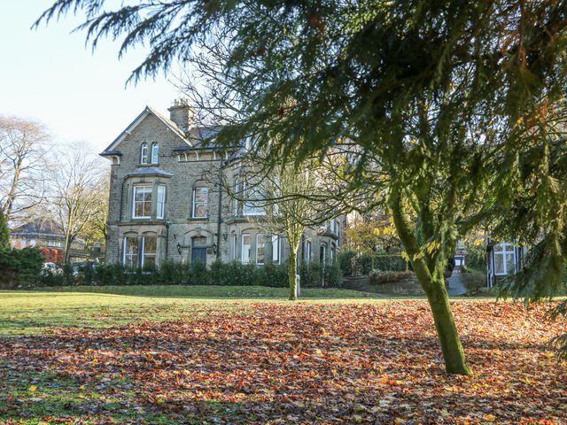 An old stone house with windows and a front door viewed from a garden with grass trees and fallen leaves at Castleton Suite in Buxton