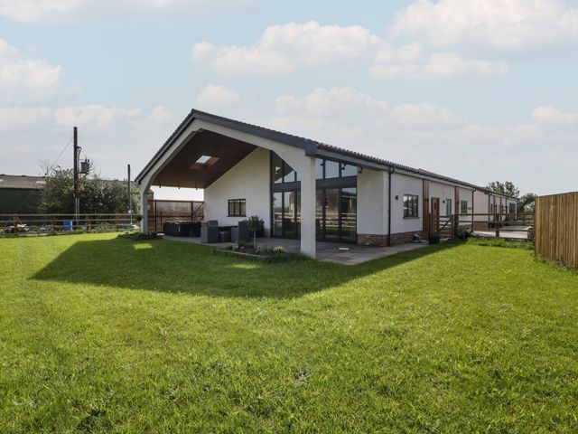 A single story house with a covered patio and outdoor seating on a grassy yard at Hidden Well in Aust