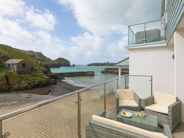A balcony with outdoor seating and drinks overlooking a rocky beach and sea at Guinevere in Mullion