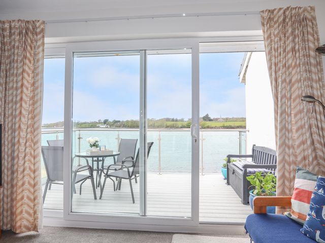 A balcony with glass table and chairs overlooking a body of water and countryside at Waters Edge Ymyl Y Dwr in Y Felinheli