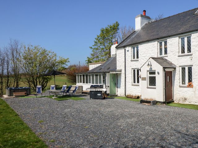 A white stone house with a gravel driveway outdoor chairs a table a barbecue and a hot tub at Ty'n Pwll Farm in Nefyn