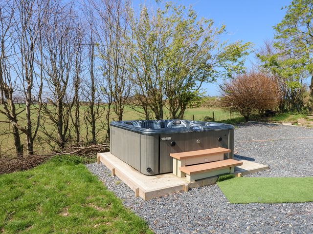 An outdoor hot tub with steps on a concrete base surrounded by gravel and grass at Ty'n Pwll Farm in Nefyn