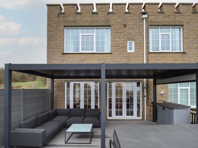A patio area with gray sectional sofa and glass coffee table under a black pergola at Castle Top Haven in Nettleton Top near Caistor