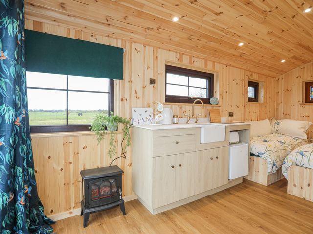 A wooden room with a small kitchen area a heater a plant and two beds at Tal Sarn Shepherd Hut in Dwyran near Niwbwrch Newborough