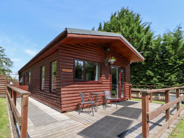 A wooden cabin with a deck and chairs at The Fallows Llanerch Park near St Asaph
