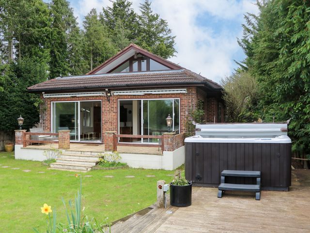 A brick house with a patio garden and a hot tub on a wooden deck at Coventina in Wraysbury