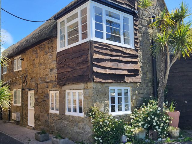 An exterior view of a cottage with a thatched roof and wooden panels at Fishermans Locker, West Bay