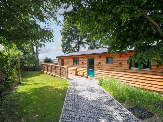 A cabin with a pathway leading to a door surrounded by grass and trees at Owl Lodge Menheniot