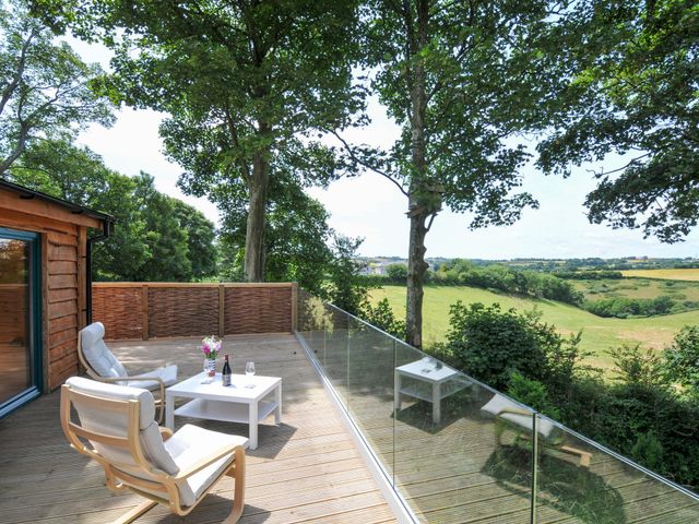 A deck with chairs and a table overlooking fields at Owl Lodge in Menheniot
