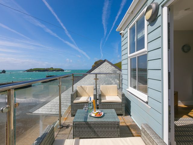 A balcony with wicker chairs a table with drinks and snacks overlooking the sea at Demelza Mullion Cove near Mullion