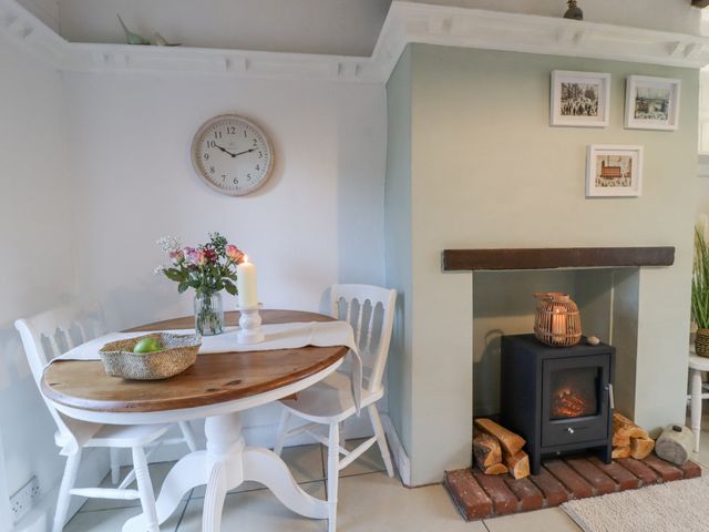 A dining area with a wooden table and white chairs next to a fireplace with a wood stove at Penny Cottage in Haworth
