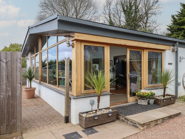 A small building with large windows wooden frames potted plants and a doorway leading inside at Burlodge Swimbridge near Barnstaple