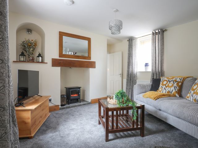 A living room with a sofa, coffee table, television on a stand, and a small fireplace at Islwyn Bryn Pydew near Llandudno Junction