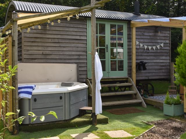 An outdoor area with a hot tub and wooden steps leading to a structure with green double doors at Burr 1 Shepherds Hut in Barnstaple