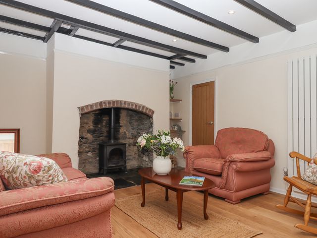 A living room with a wood stove fireplace pink armchairs wooden coffee table flowers and a rocking chair at Glebe Cottage in Buckland Monachorum near Yelverton