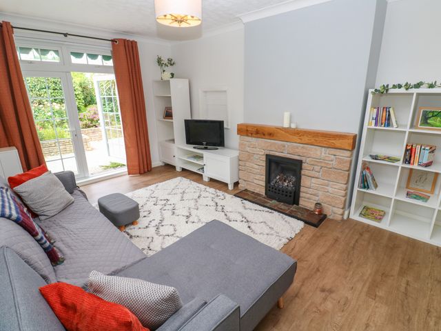 A living room with a gray sofa a white rug a stone fireplace a white shelving unit and glass doors leading outside at Alexandra Close Illogan